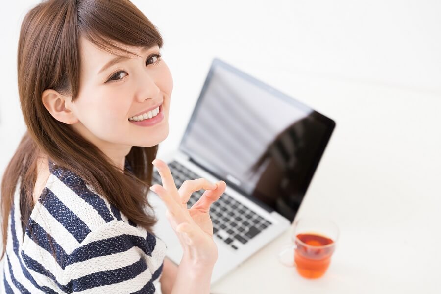 パソコンの前でOKマークを作る笑顔の女性